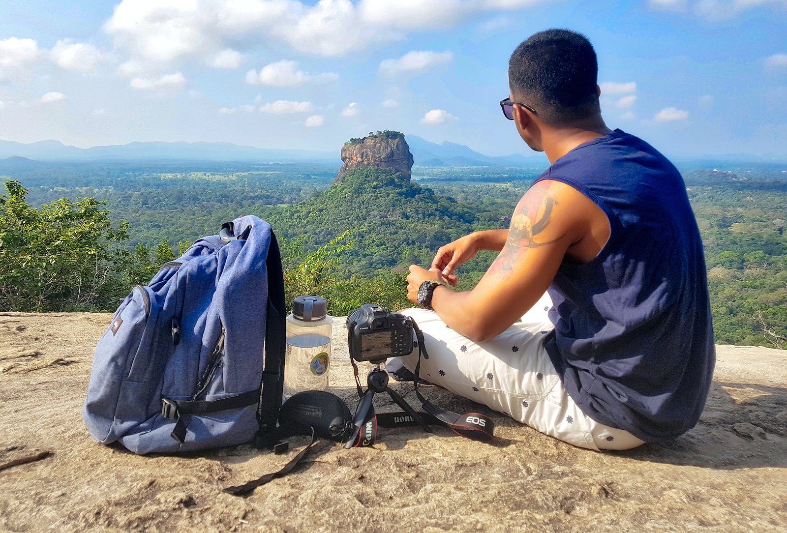 Man Sitting on Top of Gray Cliff Mountain Beside Backpack, Water Bottle, and Camera 24 oz vs 32 oz Water Bottle